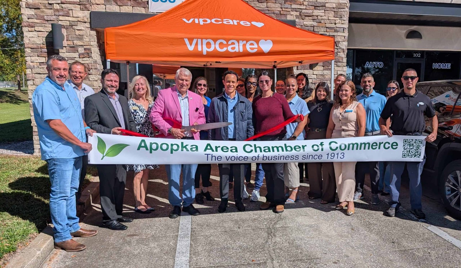 1. A diverse group of business professionals holding a ribbon in front of an Apopka Area Chamber of Commerce event, promoting local business growth and community engagement.